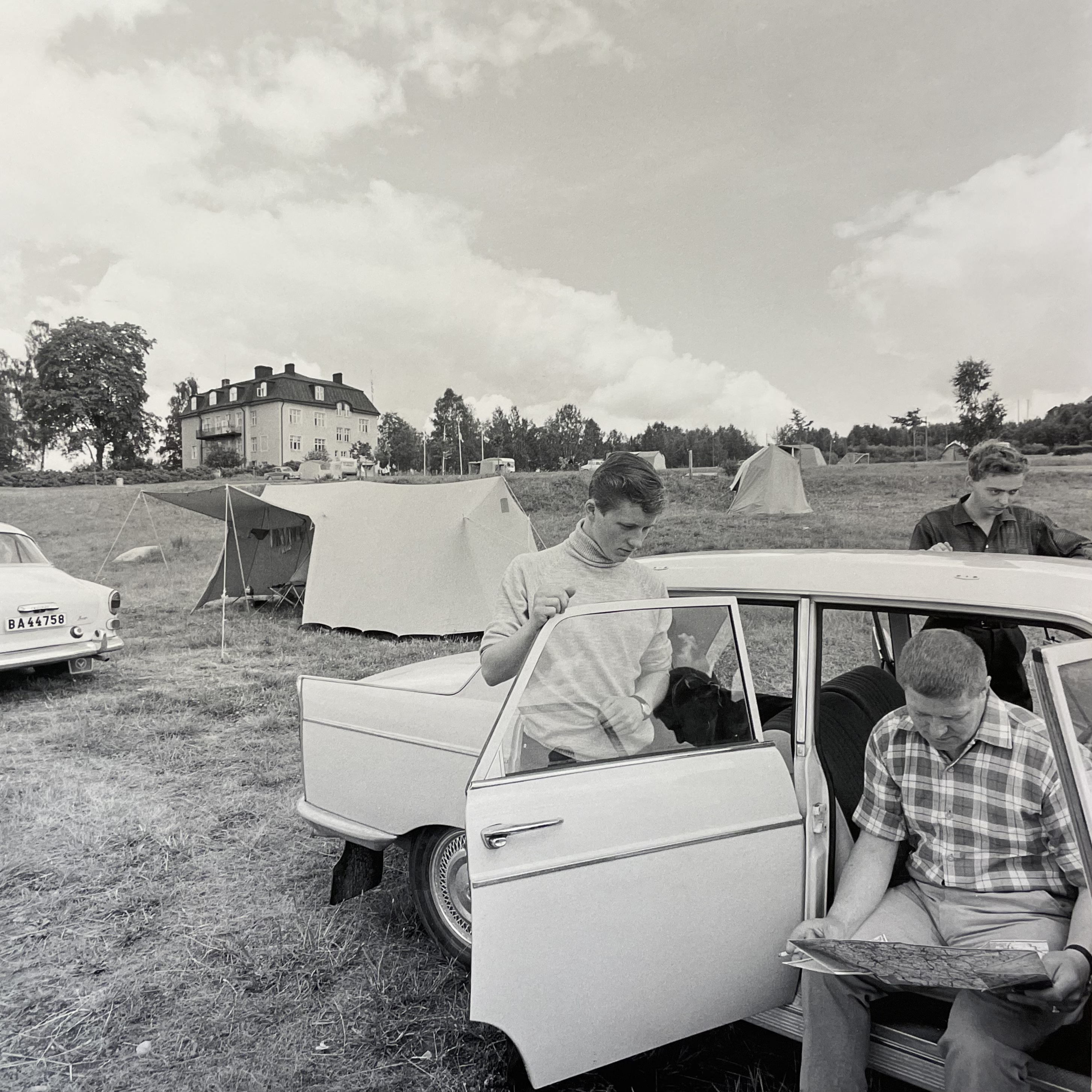 Svartvitt fotografi på tre killar som har stannat sin bil för att läsa kartan Svartvitt fotografi på tre killar som har stannat sin bil för att läsa kartan